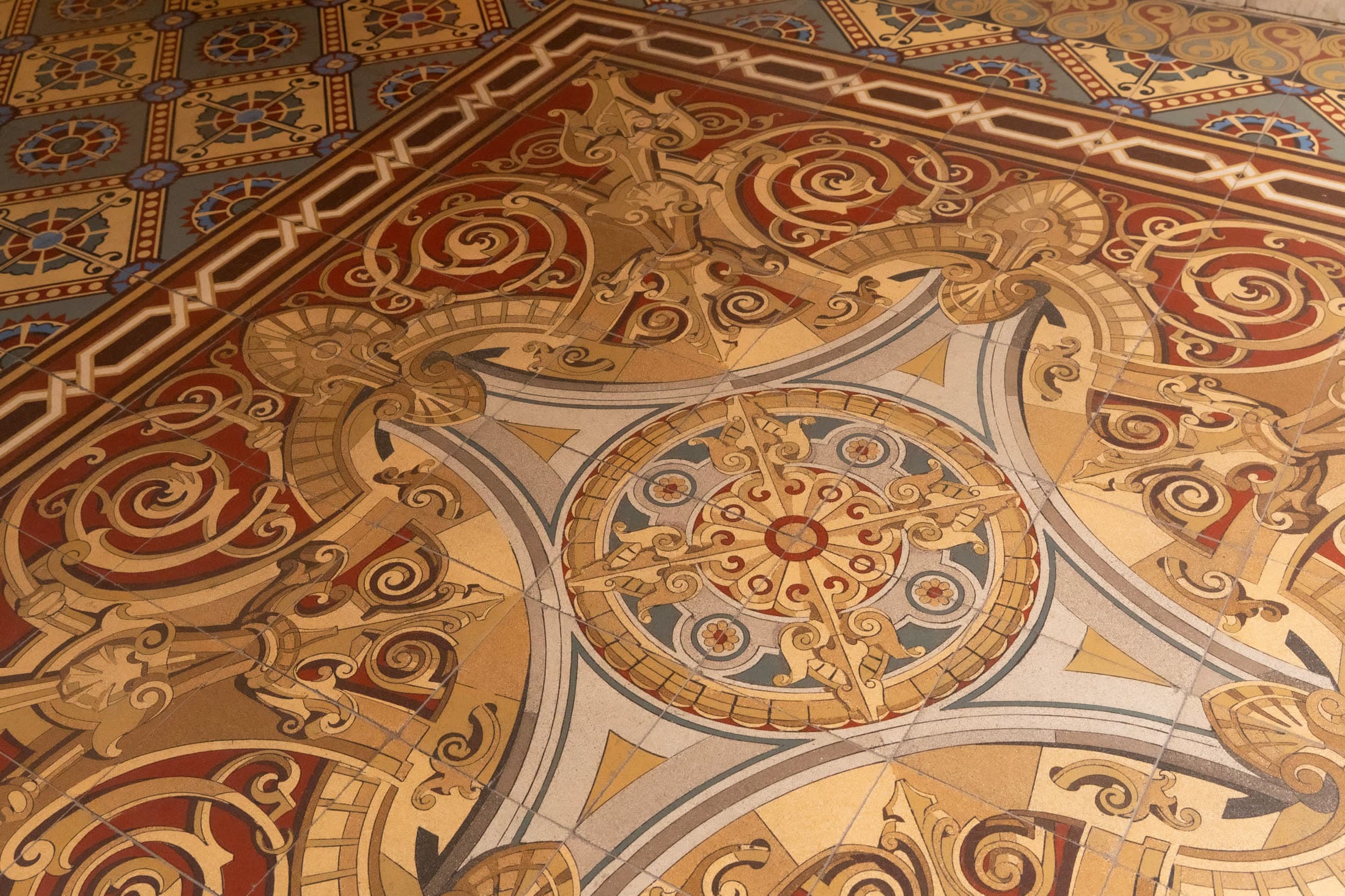 Piso histórico com mosaico ornamental em tons de dourado, vermelho e azul